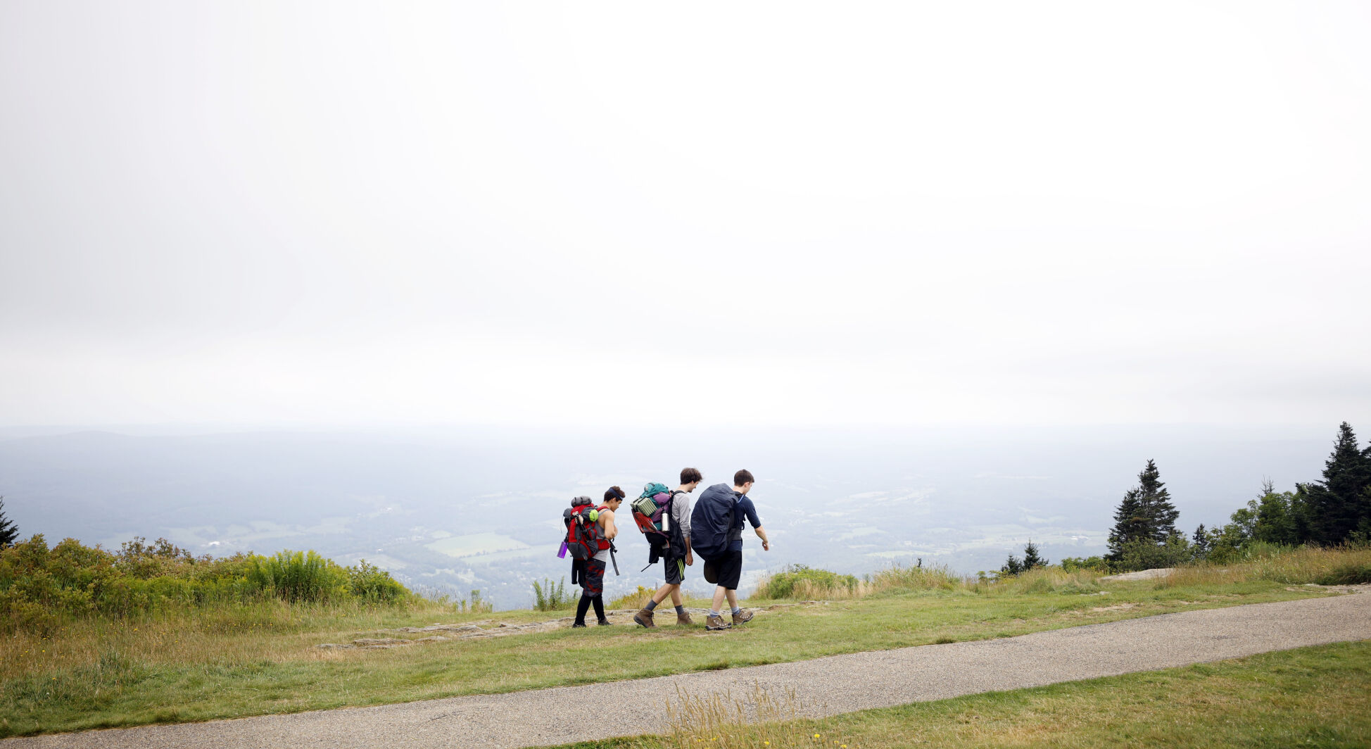 Three men hike with backpacks at the top of Mount Greylock